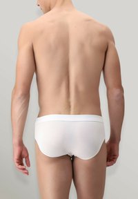 Slip di cotone bianchi con una texture liscia, vita media e design minimalista, visti dal retro. Sfondo grigio chiaro.