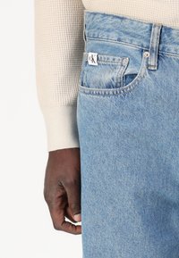 Jeans in denim azzurro chiaro con vestibilità classica, dotati di un'etichetta con il logo CK, dettagli sulle tasche anteriori e una texture tessuta sottile.