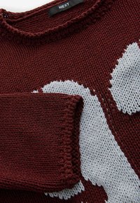 Burgundy stickad tröja med ett grått abstrakt mönster, rund hals, och strukturerad tyg med synlig sömnad och vävdetaljer.