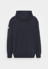 Námořnická modrá mikina s kapucí na šňůrku, pružnými manžetami a lemem. Na levém rukávu je malá značka. Hladká textura látky.