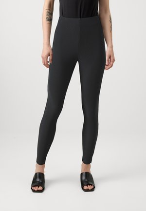 Leggings noirs taille haute en tissu texturé, au design ajusté et à la construction sans coutures. Associés à des sandales à glissière noires simples.