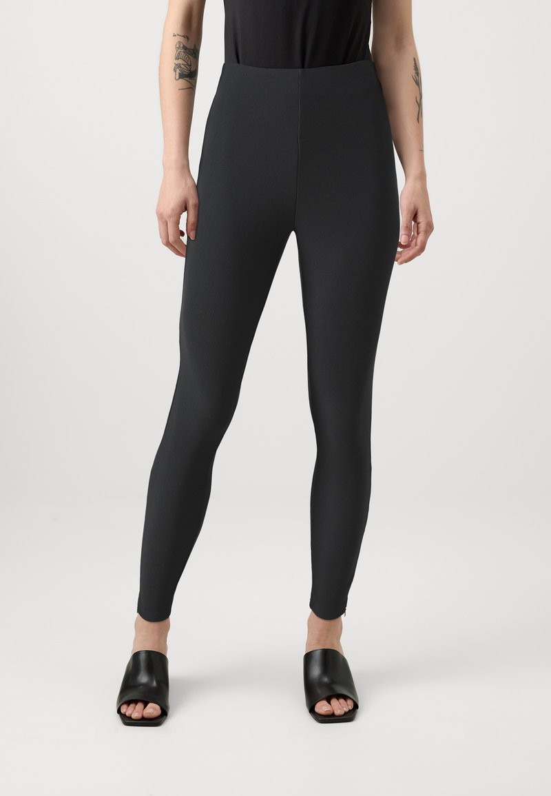 Leggings noirs taille haute en tissu texturé, au design ajusté et à la construction sans coutures. Associés à des sandales à glissière noires simples.