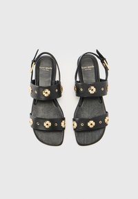 Juodos odinės šlepetės su auksinėmis gėlių detalėmis ir studs, su dviem plačiomis dirželių juostomis ir slingback dizainu, leidžiančiu reguliuoti tinkamumą.