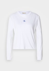 Maglietta bianca a maniche lunghe in cotone con scollatura rotonda. Presenta un piccolo logo ricamato "cK" blu sul petto. Design semplice.