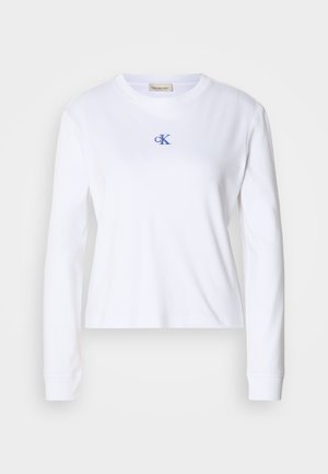 Camiseta de manga larga blanca de algodón con cuello redondo. Presenta un pequeño logo bordado "cK" en azul en el pecho. Diseño simple.