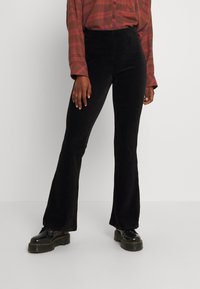 Svarta kordflorsbyxor med en texturerad tyg, med hög midja och en slät, åtsittande passform ner till knäna. Kombineras med platåskor.