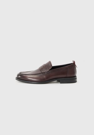 Brown leather loafers with a rounded toe, stitched detailing, and a small red accent at the heel. Flat rubber sole.