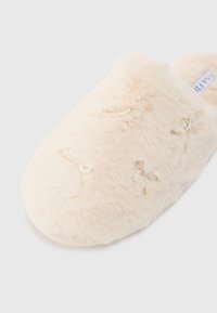 Chinelo de pelúcia sintética em bege claro com detalhes de laço em conta. Textura suave e forma arredondada para conforto.