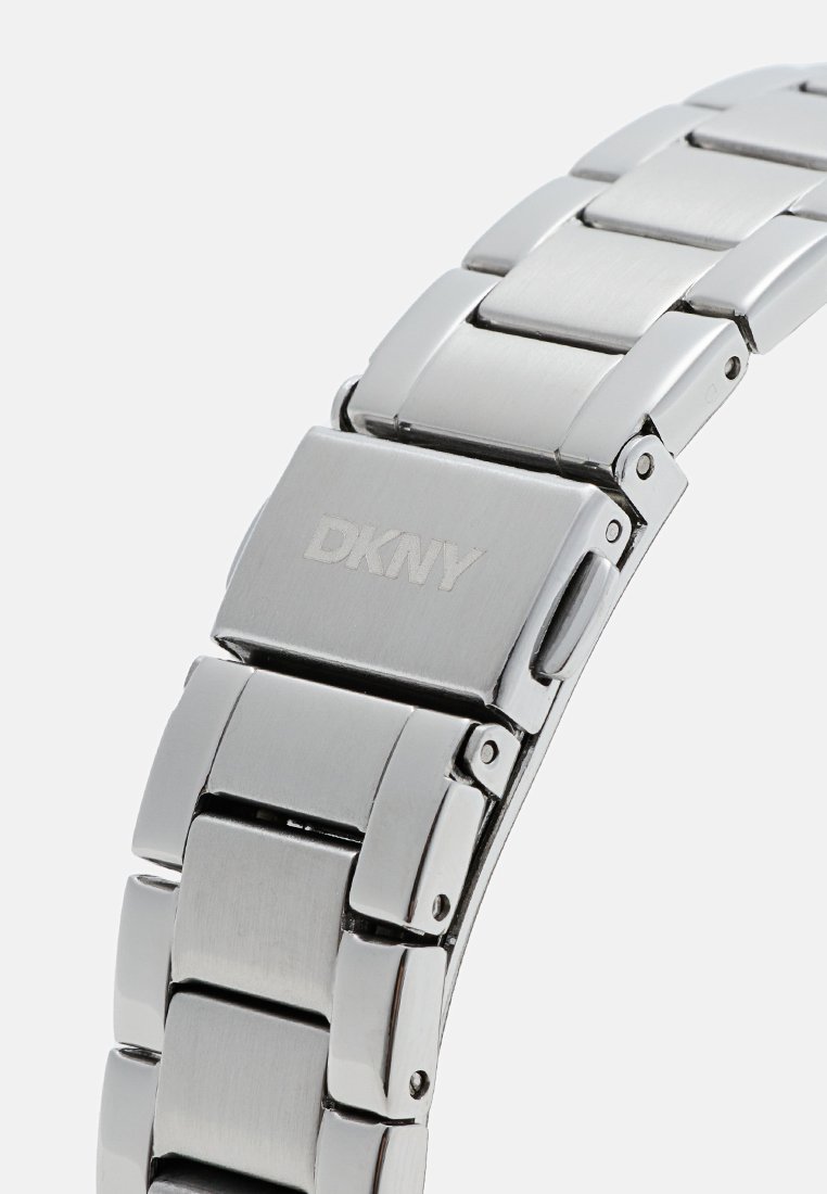 Bracelet de montre en acier inoxydable argenté DKNY avec une finition polie, présentant des maillons rectangulaires et un fermoir avec un logo gravé.