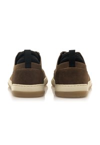 Scarpe in suede marrone con un collare imbottito nero, intersuola bianca e suola in gomma texturizzata color tan. Presentano anche due linguette di trazione sul tallone.