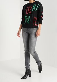 Černá mikina s vícbarevnými grafickými písmeny, doplněná úzkými šedými džíny a černými kotníkovými botami, s hladkou texturou.