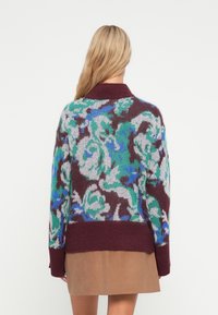 Maglione oversize in misto lana con un motivo floreale blu, verde e grigio su uno sfondo bordeaux scuro, dotato di polsini e colletto a coste.