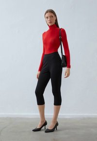 T-Shirt vermelho de manga longa com gola alta, combinado com leggings pretas até ao joelho e saltos altos pretos, equilibrado com uma pequena mala de ombro preta.