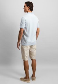 Lyseblå poloskjorte med korte ermer, kombinert med kremfargede shorts. Plagget har klassisk krage og subtile sidespalter.