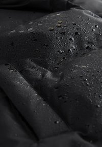 Gros plan d'un tissu imperméable noir avec des gouttes d'eau sur sa surface texturée.