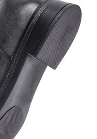 Stivale in pelle nera con suola spessa e texture e finitura liscia. Il tacco ha una forma rettangolare con una leggera curvatura.