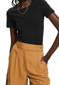 Zwarte, aansluitende t-shirt met korte mouwen, gecombineerd met hoogwaardige, beige geplooide shorts met knoopsluiting en zijzakken.