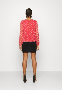 Blusa floral vermelha com mangas longas transparentes e design peplum, combinada com uma saia preta justa e sandálias de salto preta. Vista traseira.