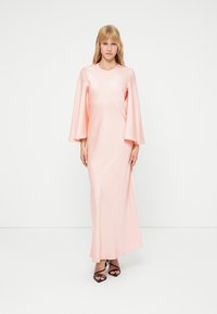 Ροζ σατέν μάξι φόρεμα με φαρδιά μανίκια, στρογγυλή λαιμόκοψη και λεία υφή. Σε συνδυασμό με μαύρα σανδάλια ανοιχτού τύπου. Μινιμαλιστικός σχεδιασμός.