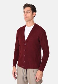 Cardigan bordeaux a coste con scollo a V, sei bottoni e coulisse regolabili. Realizzato in tessuto a maglia testurizzato.