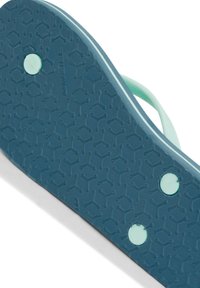 Sininen kuminen sandaalin pohja, jossa on teksturoitu pinta hexagonaalisilla kuvioilla ja kaksi pyöreää vihreää aksenttia lähellä keskustaa.