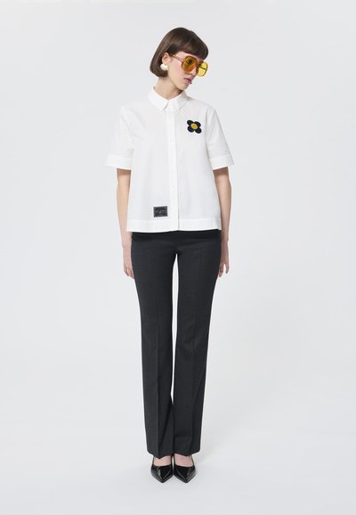 Witte shirt met korte mouwen met een zwart en gele bloemenapplicatie, gecombineerd met donkergrijze broek en zwarte puntige hakken.