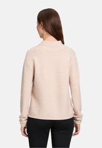 Rosa ribbad tröja med långa ärmar och hög krage. Texturen har horisontella ränder och passformen är avslappnad.