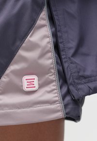 Μωβ ελαφριά αθλητικά σορτς με λεία υφή, με αντίθετες ανοιχτό ροζ και γκρι λεπτομέρειες, που διαθέτουν ένα ετικέτα με λογότυπο στο στρίφωμα.