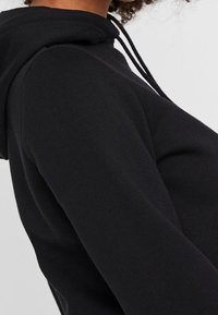 Schwarzer Kapuzenpullover mit weicher Textur, Kordelzug-Details und enganliegenden Ärmeln, der ein minimalistisches Design betont.