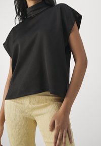 Top negro de cuello alto con mangas cortas, hecho de material suave. Combinado con pantalones cortos de textura amarilla clara.