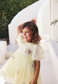 Hellgelbes Kleid mit floraler Stickerei, kurzen Puffärmeln und mehrlagigem Tüllrock. Glatter Stoff und lebendige Farben.