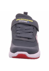Sneaker impermeabile grigia con upper in rete, lacci testurizzati e strap in Velcro. Presenta una suola bianca e rossa. Logo del marchio sulla strap.