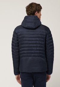 Dunkelblaue Steppjacke mit Kapuze, die ein gestepptes Design und eine glatte Textur aufweist. Sie hat elastische Bündchen und einen leicht geschwungenen Saum.