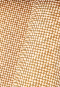 Materiał bawełniany w diagonalny wzór małych białych diamentów na jasnobrązowym tle, prezentujący gładką teksturę i błyszczące wykończenie.