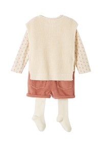 Beige Strick-Westen über einem blumigen Langarmhemd, kombiniert mit rosa Cordshorts und cremefarbenen gerippten Strumpfhosen. Merkmale sind Taschen.