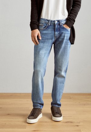 Lichtblauwe denim jeans met een rechte pasvorm, vervaagde delen en een vijf-pocket ontwerp, gedragen met een wit t-shirt en een donkere trui, gecombineerd met bruine sneakers.