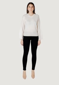 Maglione a V in maglia di un beige chiaro con un motivo geometrico testurizzato, abbinato a pantaloni neri aderenti e tacchi nude.