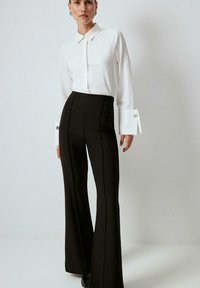White long-sleeve shirt with a collar and button details, paired with high-waisted, black flared trousers featuring side seams.