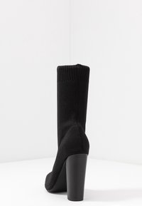 Černé pletené kotníkové boty na vysokém podpatku s vroubkovaným lemem, vyrobené z texturované tkaniny a s minimalistickým designem.