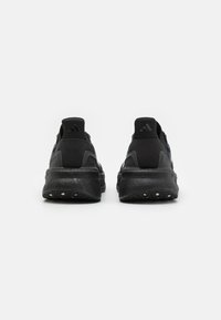 Une paire de chaussures de course Adidas noires vues de l'arrière, montrant des semelles texturées et des languettes de talon avec le logo Adidas sur un fond blanc.
