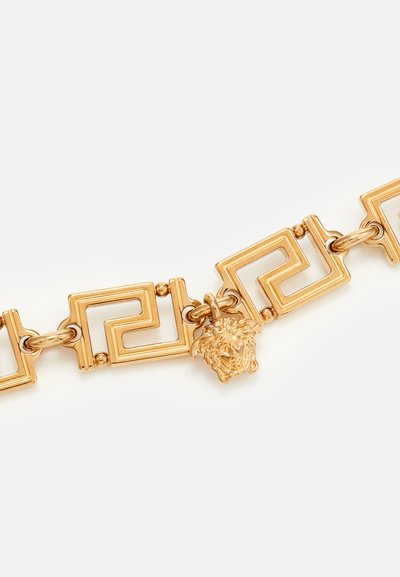 Goldfarbener Armreif mit einem geometrischen Design aus quadratischen Gliedern und einem Löwenkopf-Anhänger, der glatte Metalloberflächen und filigrane Details zeigt.