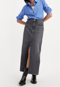 Středně dlouhá černá džínová sukně s předním rozparkem, vysokým pasem a jemnými švy. V kombinaci s modrou košilí na knoflíky a černými botami.