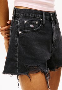 Sorte denimshorts med frynset kant, med en frontlomme med metallnagler og et lite logokort. Høyt liv.