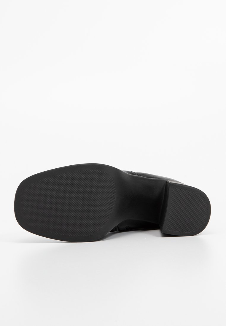 Chaussure noire à bout rond, dotée d'une semelle en caoutchouc texturé et d'un matériau supérieur lisse. Design minimaliste sans accents visibles.