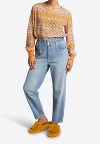 Blusa de manga larga con un vibrante patrón en naranja y blanco, combinada con unos pantalones vaqueros de tiro alto en azul claro y cómodas sandalias amarillas de tipo slide.