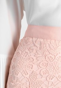 Light pink skirt with a wide elastic waistband, featuring embroidered floral patterns and a smooth texture. Complemented by a white top.