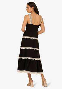 Robe maxi noire avec bordure en dentelle, présentant un corsage ajusté, un dos plongeant et un ourlet évasé. Accentuée de détails en dentelle texturée sur les bretelles.