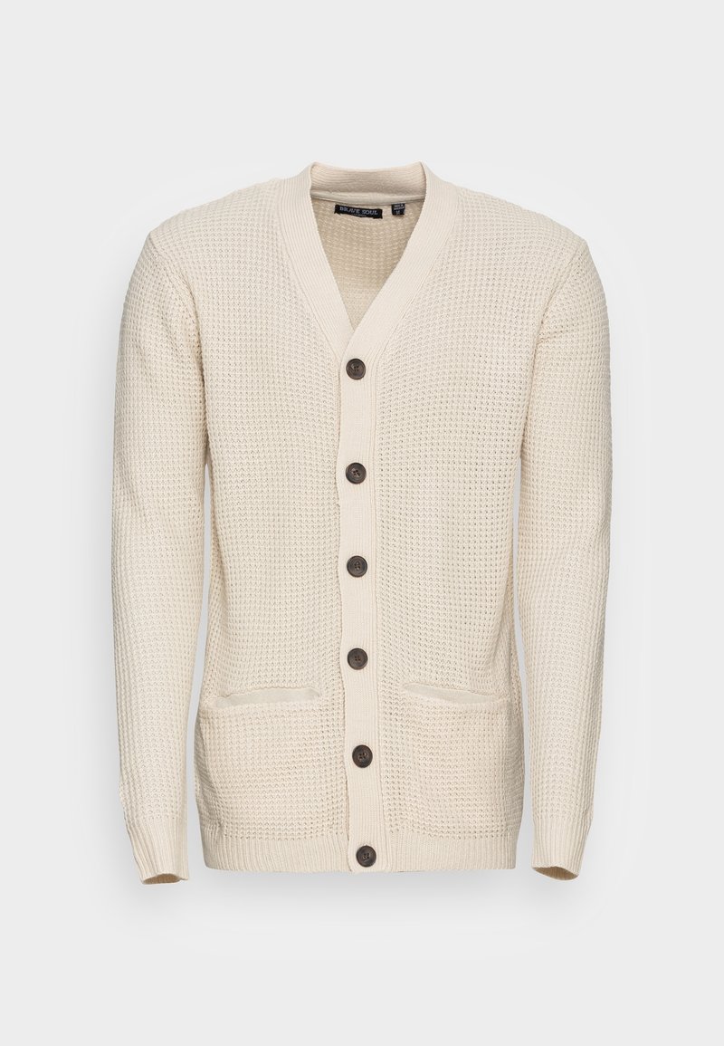 Krämfärgad stickad kofta med V-ringning, åtta mörka knappar framtill och två framfickor. Strukturerad tyg med ribbade ärmar.