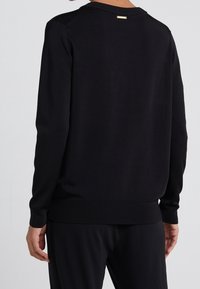 Zwarte trui met lange mouwen, ronde halslijn en geribbelde manchetten. Voorzien van een klein gouden accent bij de achterste halslijn. Soepele textuur, casual pasvorm.