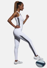 Biały sportowy podkoszulek i legginsy z czarnymi bocznymi panelami, w parze z białymi sneakersami. Modelka w dynamicznej pozie z piłką koszykową.